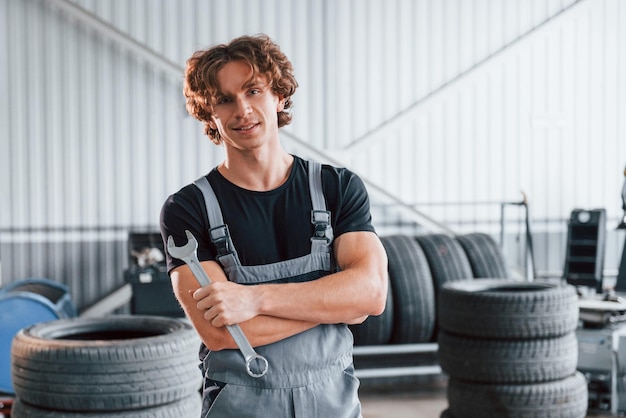 Con la herramienta en la mano un hombre adulto con uniforme de color gris trabaja en el salón del automóvil