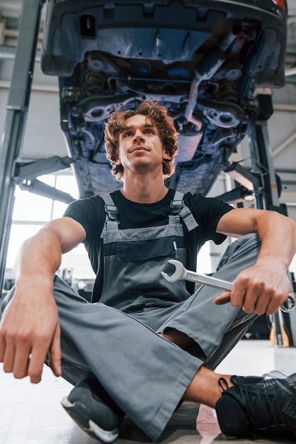 Con la herramienta en la mano Un hombre adulto con uniforme de color gris trabaja en el salón del automóvil