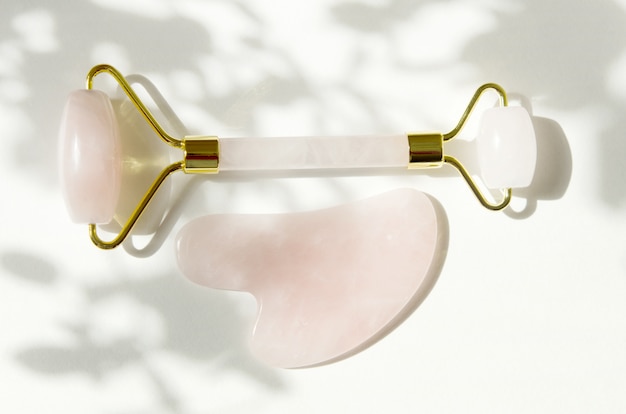 Herramienta de masaje Pink Gua Sha. Rodillo de cuarzo rosa. Sombra gris de las hojas. Cuidado facial de la piel en el hogar, terapia antienvejecimiento y lifting.