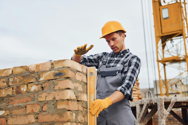 Con herramienta de medición de nivel Trabajador de la construcción en uniforme y equipo de seguridad tiene trabajo en la construcción