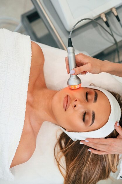 herramienta de terapia eléctrica rostro de mujer recibiendo cuidado facial por manos de esteticista en el salón de spa