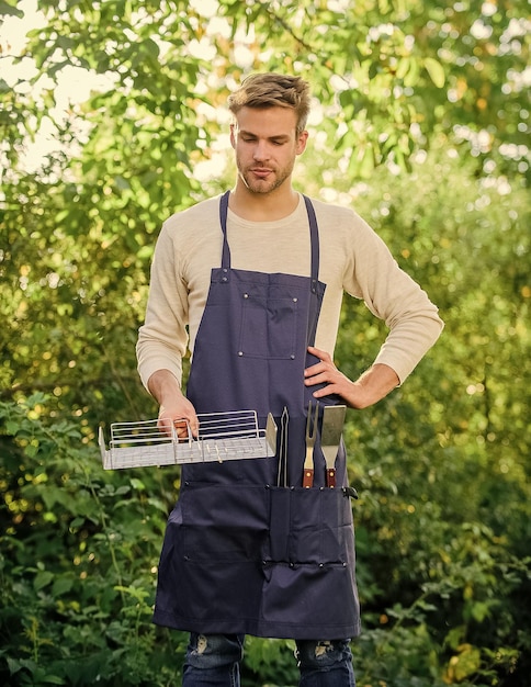 Herramientas para asar carne al aire libre Métodos asar a la parrilla Concepto de barbacoa Chico guapo cocinando comida Hombre sostiene rejilla para asar Comida a la parrilla Fiesta de barbacoa en el patio trasero Comida saludable Receta parrilla Concepto de picnic