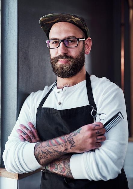 Herramientas de barbero y retrato de hombre para el cuidado del cabello, bienestar y peine para el servicio de barba, brazos cruzados profesionales y persona en barbería, peluquería y salón de belleza o peinado.