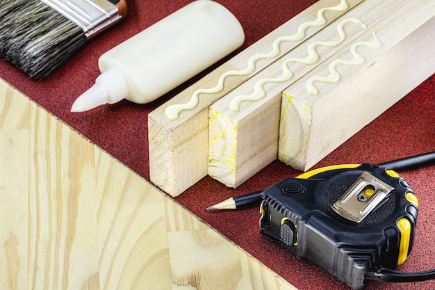 Herramientas de carpintería sobre tabla de madera, pegamento, lápiz, cinta y papel de lija