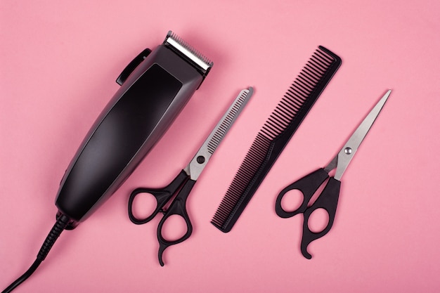 Herramientas de corte de pelo en una vista superior de fondo rosa, cortapelos y tijeras.