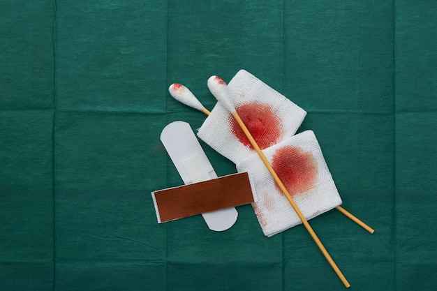 Las herramientas incluyen yesos, hisopos y gasas de sangre en un vendaje quirúrgico verde para una herida limpia