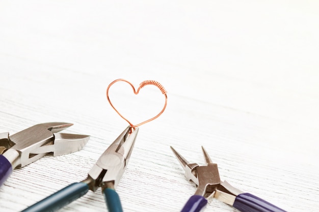 Herramientas de joyería en mesa de madera blanca. Corazón hecho de alambre de cobre. Cable enrrollado