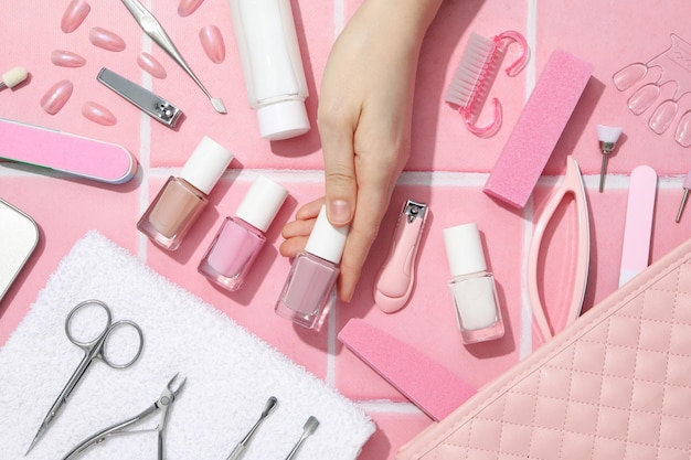 Herramientas para manicura y arte de uñas mano femenina en fondo rosa vista superior