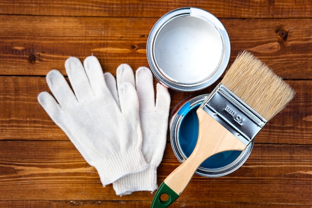Herramientas necesarias para un trabajo de pintura: pincel, cubo de pintura, guantes protectores sobre tablas de madera