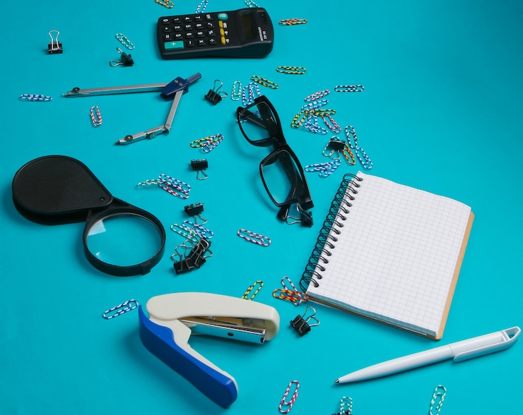 Foto herramientas de oficina, papelería. grapadora, calculadora, lupa, clips, cuaderno, brújula en azul.