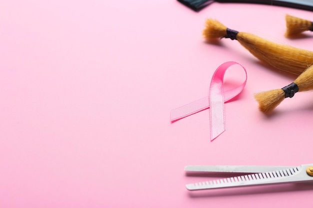 Herramientas de peluquería y cinta rosa en la superficie de color. Concepto de donación de cabello para pacientes con cáncer de mama