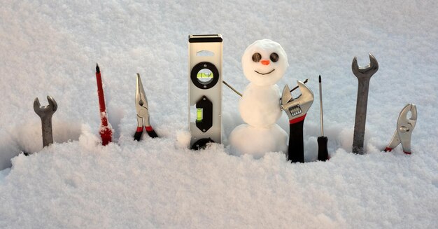Herramientas de reparación de constructor. Pequeño muñeco de nieve con instrumento de reparación. Trabajador del hombre de nieve.