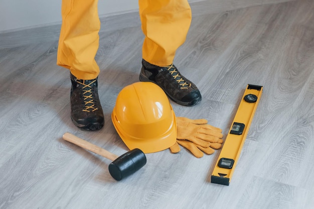 Herramientas en el suelo Manitas en uniforme amarillo de pie en el interior Concepción de renovación de la casa