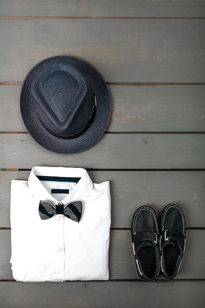 Herren-Outfit auf Holzhintergrund, Kindermode-Kleidung, grauer Fedora, weißes Hemd, Bootsschuhe für Jungen, Draufsicht, flache Lage, Kopierraum.