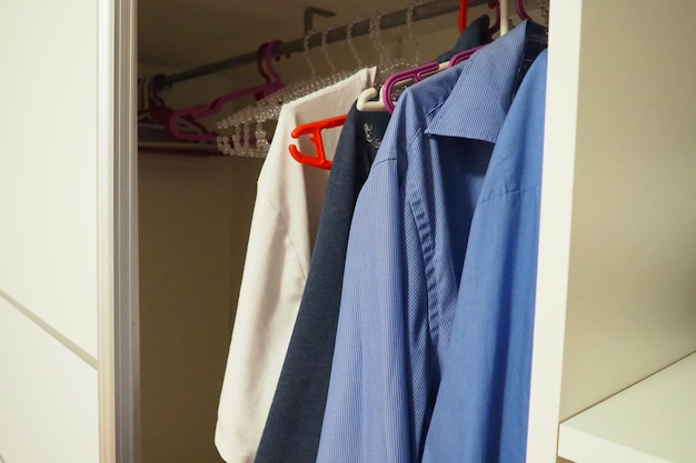 Herrenhemden hängen auf Kleiderbügeln in einem offenen weißen Schrank Herrenmode Organisation der Dinge in einem Schrank oder Ankleidezimmer Blaue und weiße Hemden Haushaltsführung