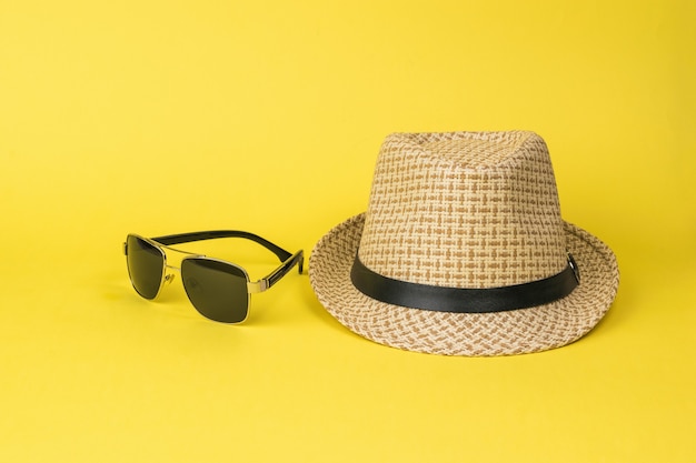 Herrensommerhut und -sonnenbrille auf gelbem Grund. Accessoires für Männer.