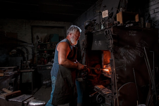 Foto herrero artesano en delantal trabaja en herrería
