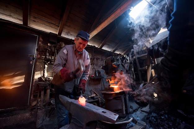 herrero forja manualmente el metal fundido al rojo vivo en el yunque en el taller de herrería tradicional. Herrero trabajando metal con martillo en la fragua