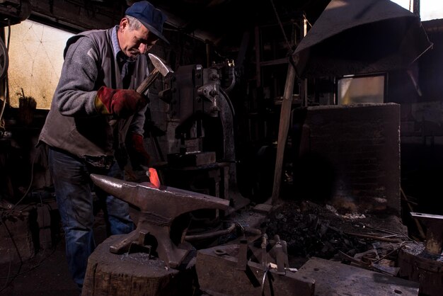 herrero forja manualmente el metal fundido al rojo vivo en el yunque en el taller de herrería tradicional. Herrero trabajando metal con martillo en la fragua