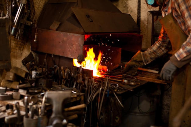 El herrero forja manualmente el metal fundido en el yunque en el taller de herrería Herrero