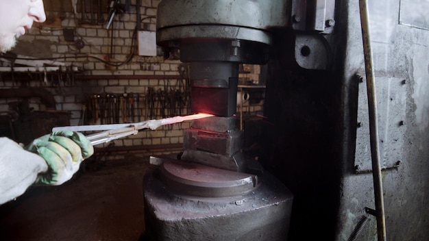 Herrero poniendo un detalle de metal caliente bajo la máquina de presión industrial