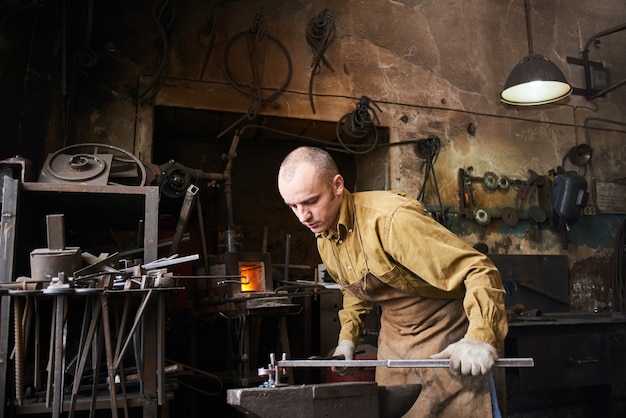 El herrero en la producción de artesanías de metal en el yunque en el taller.