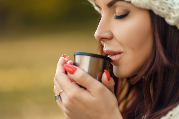 Herrliche Frau im heißen Kaffee des Hutvergnügens von der Thermosschale im kalten Herbstpark