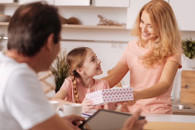 Herrlicher fröhlicher reifer Vater, der Familienurlaub zu Hause genießt und Tablette benutzt, während Frau dem Kind Geschenkbox gibt
