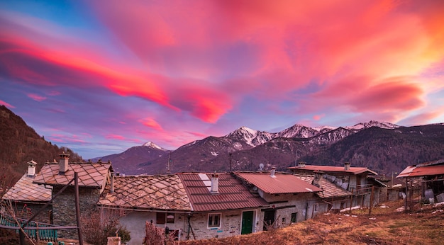 Herrlicher Sonnenuntergang in den italienischen Alpen Schöner Himmel über schneebedecktem Tal idyllisches Dorf und schneebedeckte Berggipfel Winter in Piemont Italien