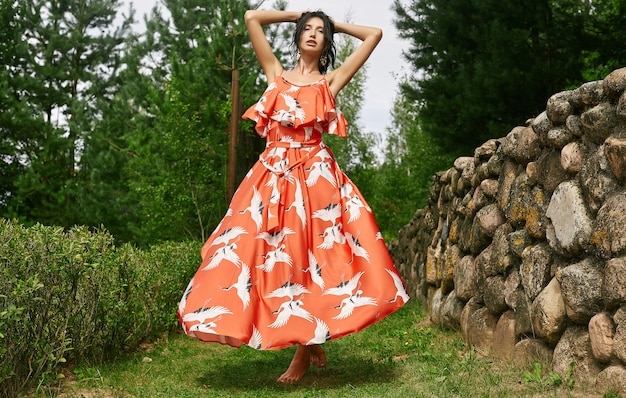 Herrliches orange Kleid der Brunettefrau in Mode im Apfelgarten