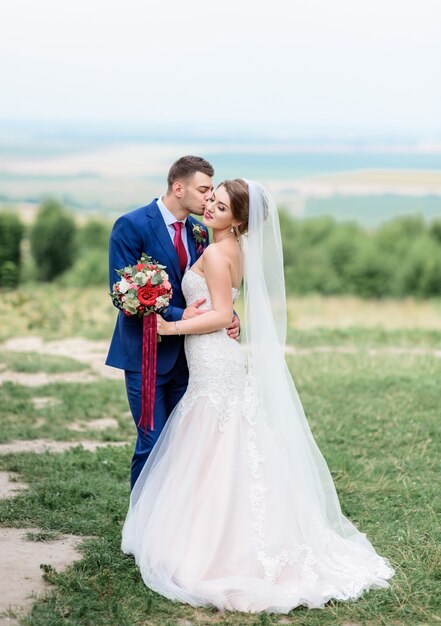 Herrliches stilvolles Hochzeitspaar steht auf dem grünen Rasen