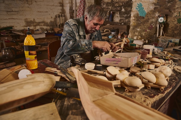 Herstellung von Holzspielzeug in der Werkstatt, Handwerker in Aktion, alter Künstler bei der Arbeit