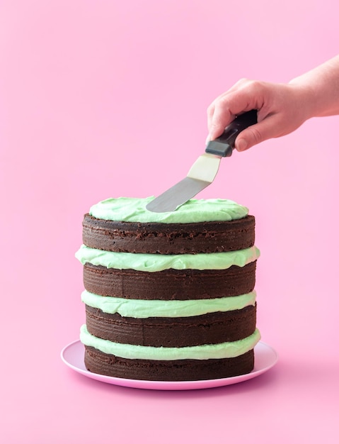Herstellung von Schokoladenkuchen mit Minzgeschmackscreme isoliert auf rosa Hintergrund
