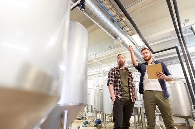 Foto herstellungs-, geschäfts- und menschenkonzept - männer mit klammern, die in einer brauerei oder einer anlage zur herstellung von alkoholfreiem bier arbeiten