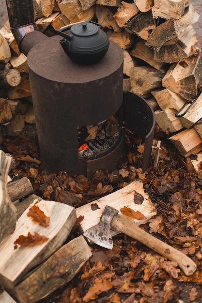 Foto hervidor de hierro fundido para la ceremonia del té oriental tradicional en la estufa quemada con hermosas hojas de roble de otoño y troncos apilados en el fondo