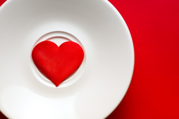 Herz auf weißem Teller am roten Hintergrund. Romantik und Liebeskonzept.