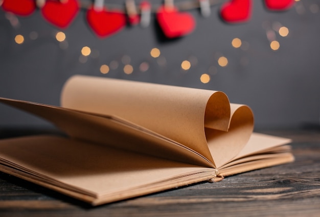 Herz aus Buchbögen in Licht, Liebe und Valentinstag Konzept auf einem Holztisch gemacht