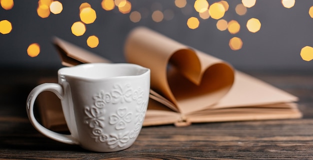 Herz aus buchbögen mit einer tasse in licht, liebe und valentinstag konzept auf einem holztisch gemacht