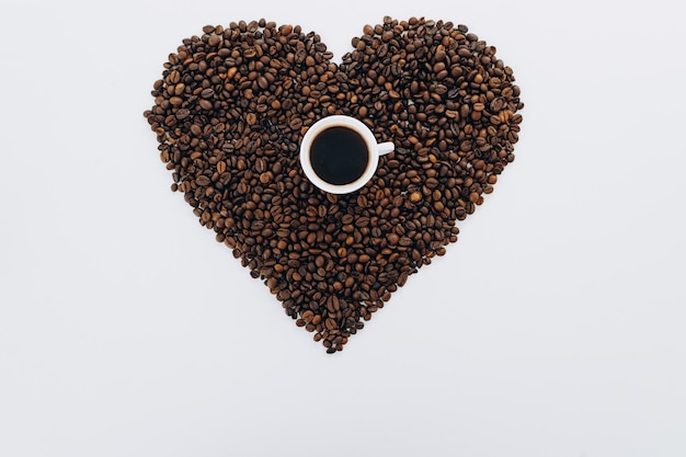 Herz aus Kaffeebohnen und gemahlenem Kaffee auf weißem Hintergrund in der Mitte ist eine Tasse