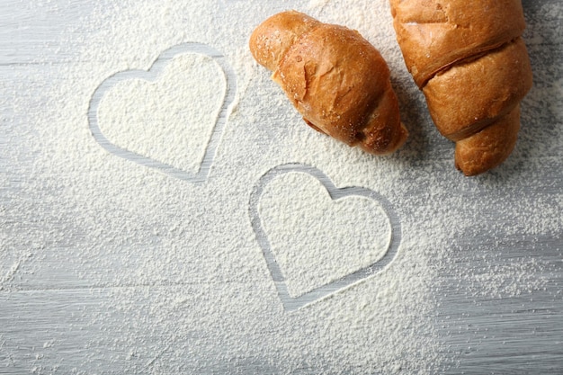 Herz aus Mehl und frischen Croissants auf Holzuntergrund
