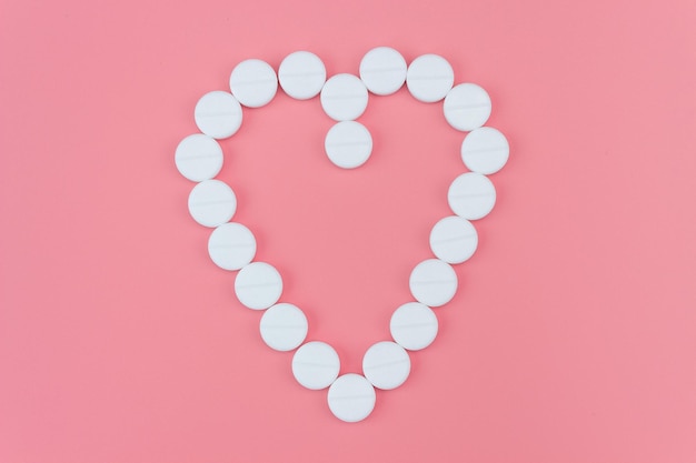 Herz aus weißen Pillen auf rosa Hintergrund.