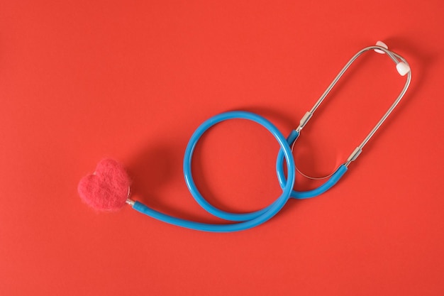 Herz aus Wolle und ein medizinisches Stethoskop auf leuchtend rotem Hintergrund