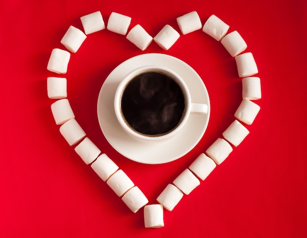 Herz des Marshmallows und einer Tasse Kaffee auf rotem Textilhintergrund. Valentinstag