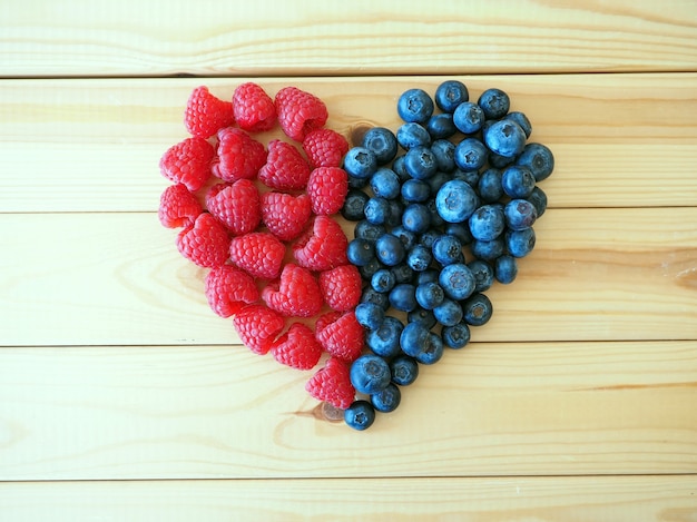 Herz gemacht von Himbeeren und Blaubeeren auf hölzernem Hintergrund