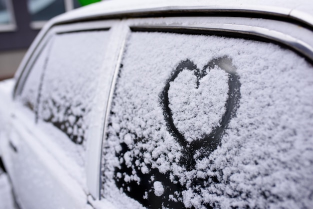 Herz gezeichnet auf einer Autowindschutzscheibe, die mit frischem Weihnachtsschnee bedeckt ist