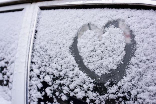 Herz gezeichnet auf einer Autowindschutzscheibe, die mit frischem Weihnachtsschnee bedeckt ist