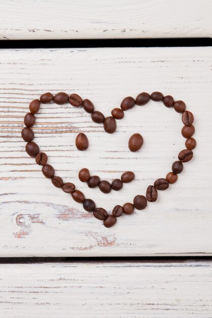 Herz-Smiley aus Kaffeebohnen. Weißes Holz auf der Oberfläche.