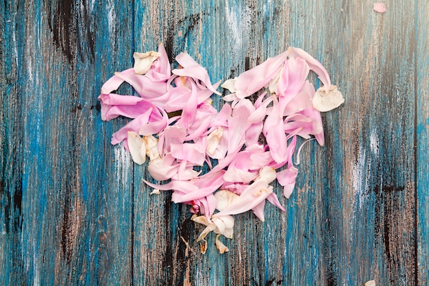 Herz von rosa und weißen Blumenblättern auf einem Holztisch. Valentinstag oder Hochzeitskonzept