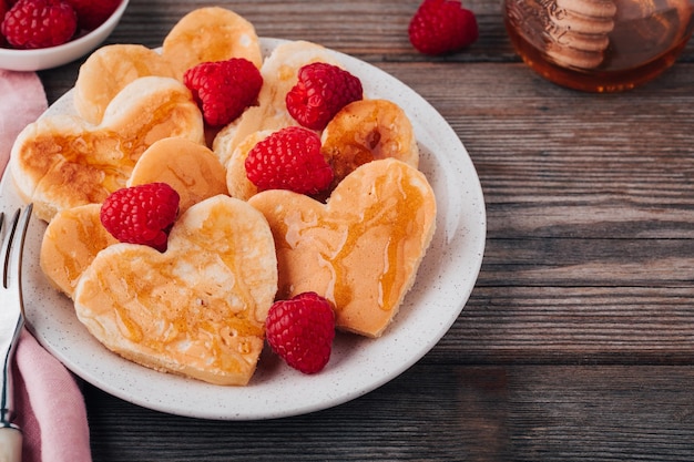 Herzförmige Pfannkuchen mit Himbeeren und Honig zum Valentinstag auf Holzboden