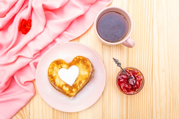 Herzförmige Pfannkuchen zum romantischen Frühstück mit Erdbeermarmelade und schwarzem Tee